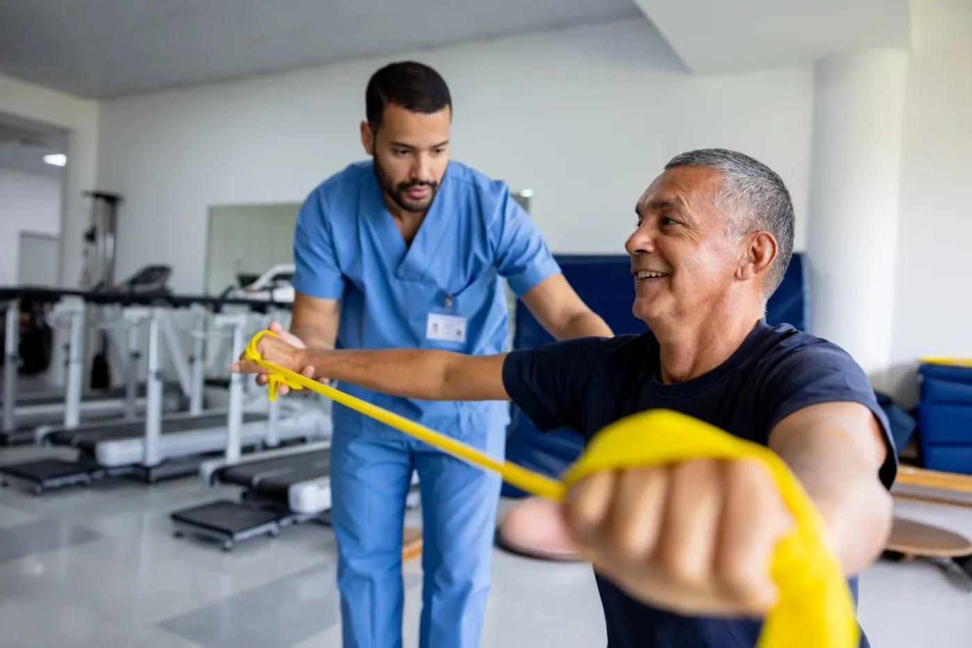 Physiotherapist helping a smiling older man with a resistance band exercise