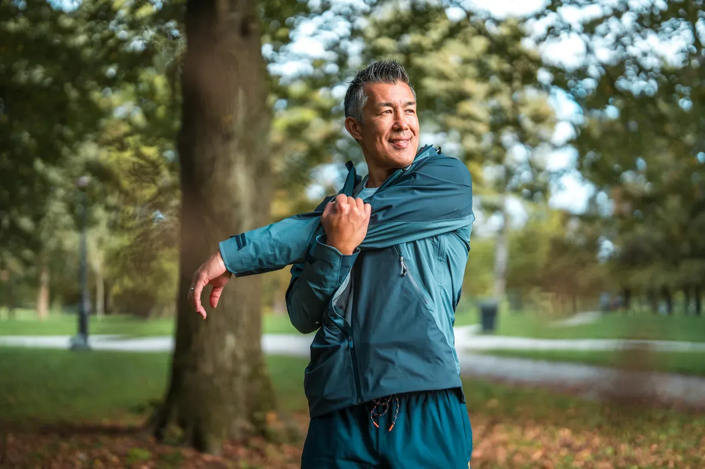 Grey-haired man stretching his shoulder in a park