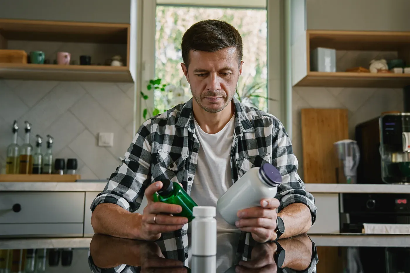 Man reading labels on supplement bottles at a kitchen counter