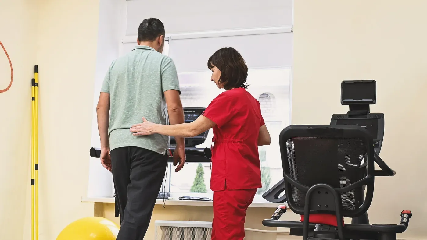Physical therapist guiding a middle-aged man walking on a treadmill