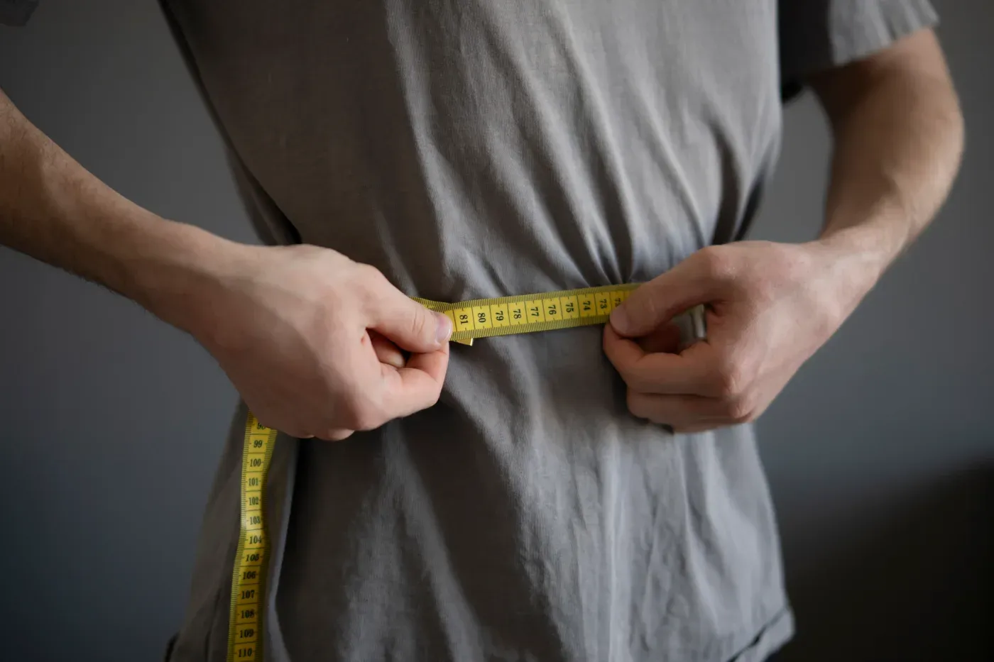 Man wrapping a measuring tape around his waist over a grey T-shirt