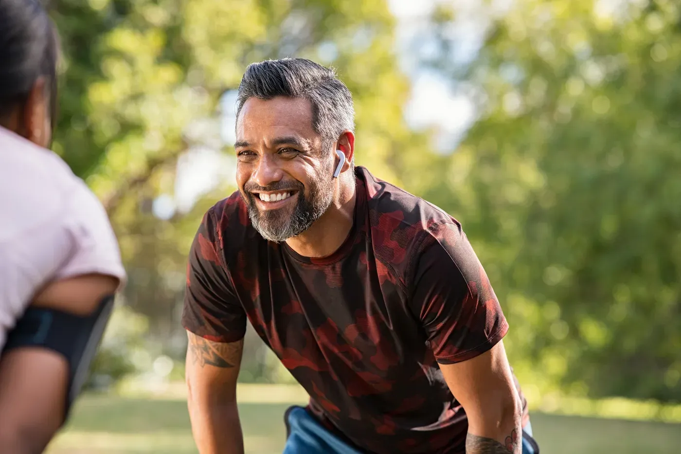 Smiling grey-bearded man resting after a jog in a sunny park