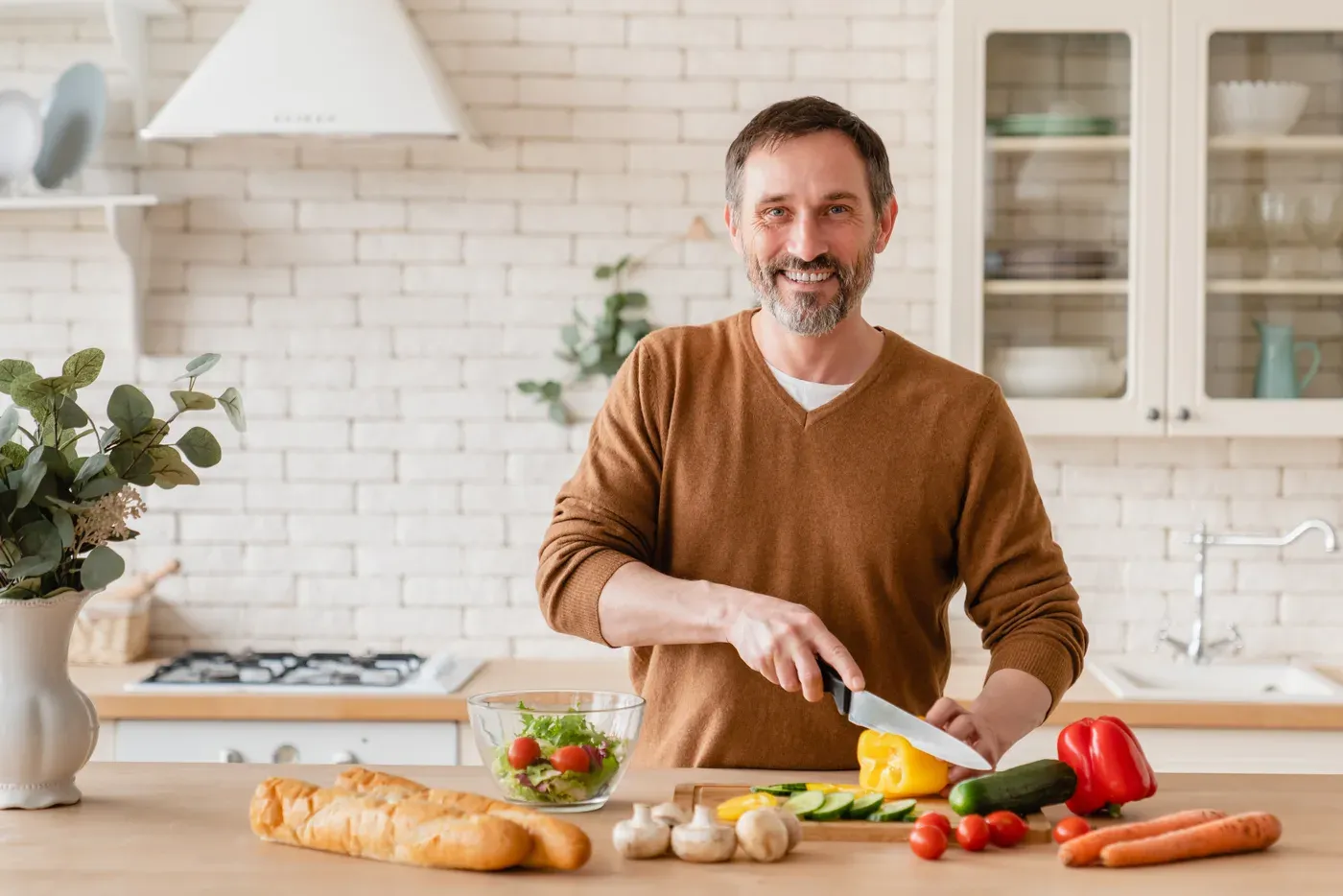 Smiling bearded man chopping vegetables for a salad in a bright kitchen