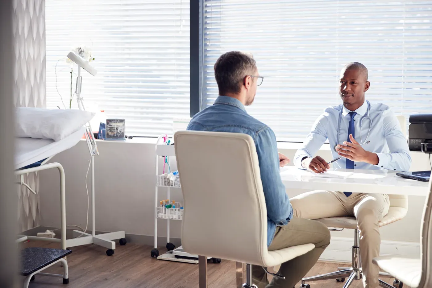 Man in a denim shirt talking with his doctor across a clinic desk