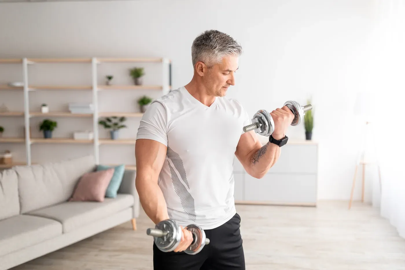 Grey-haired man doing dumbbell curls in his living room