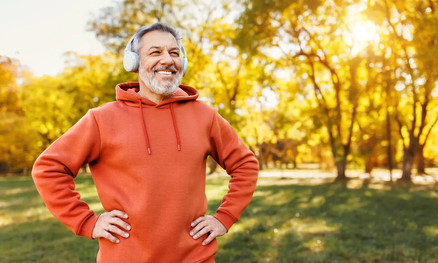 Smiling grey-bearded man in headphones and an orange hoodie in an autumn park