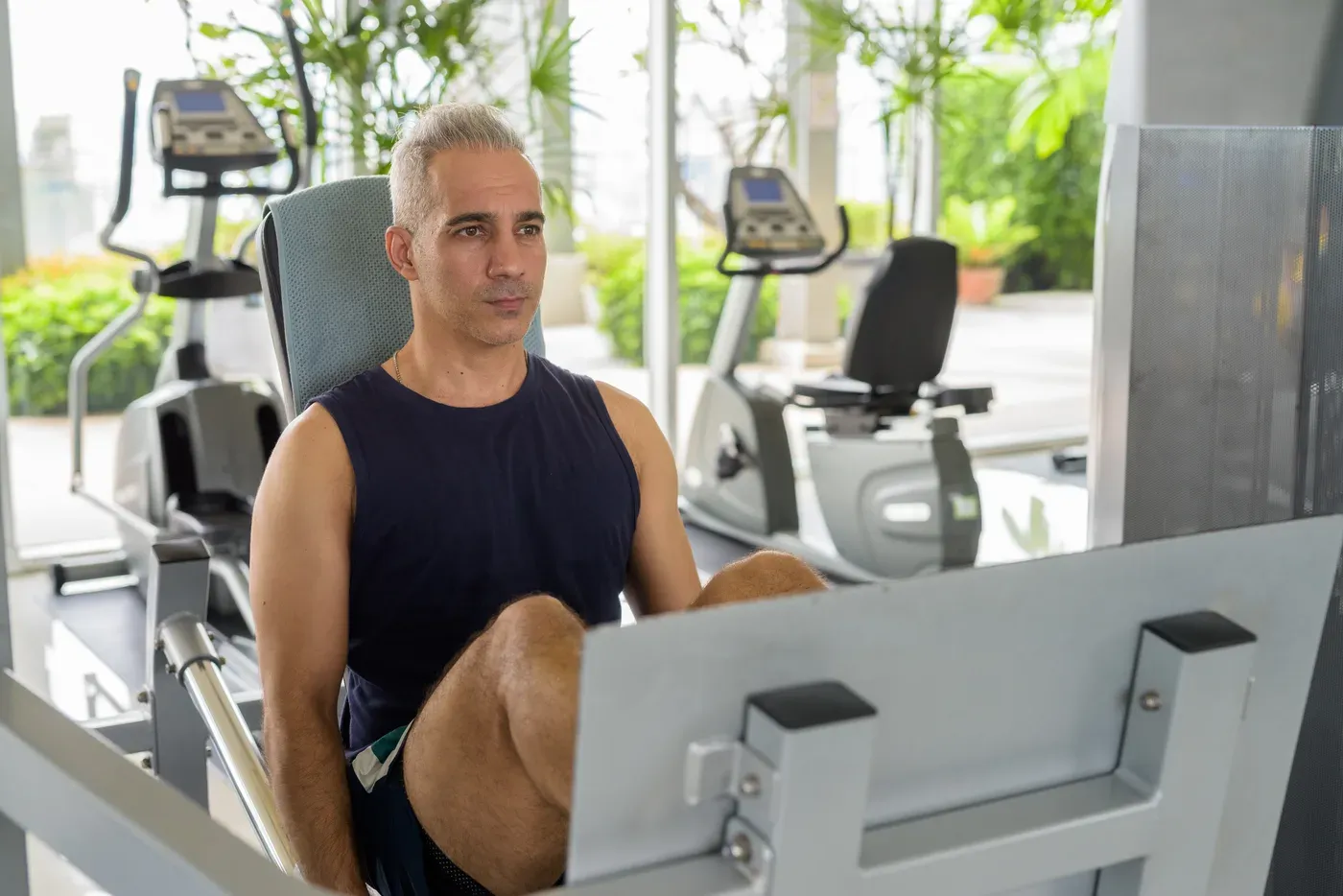 Grey-haired man using a leg press machine in a bright gym