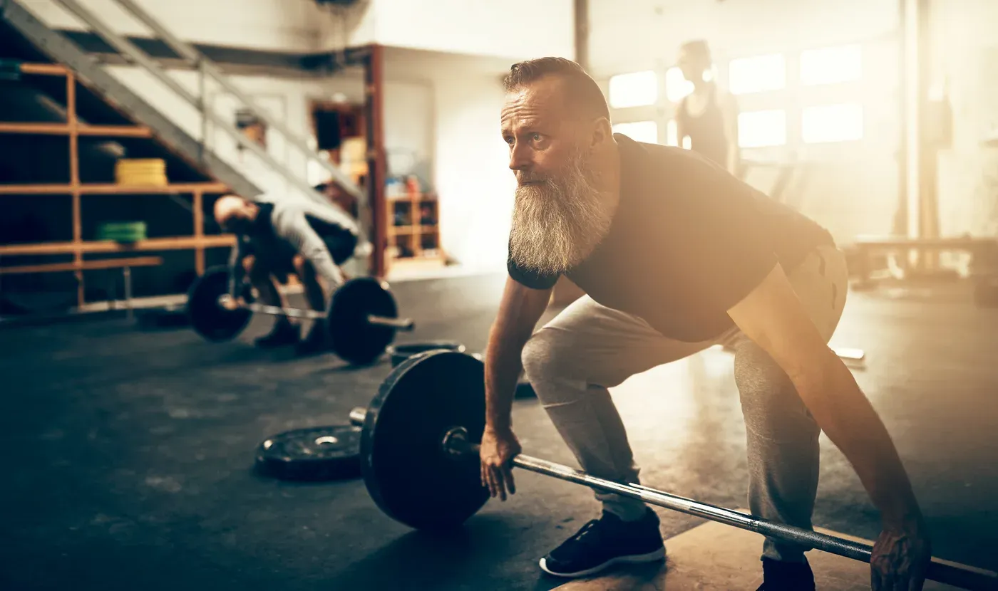 Long-bearded older man setting up for a barbell deadlift in a gym