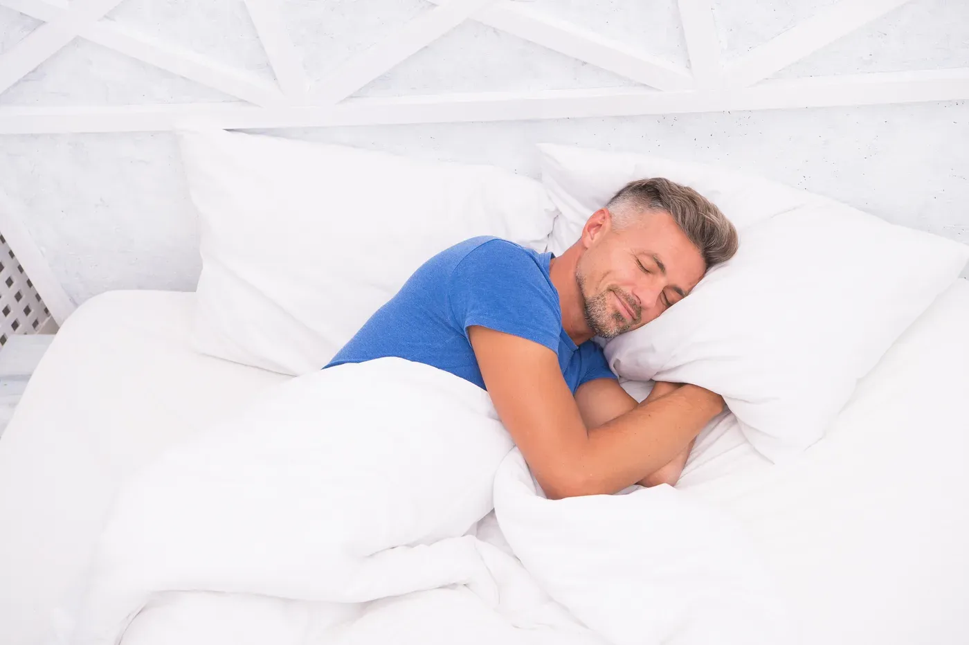 Grey-haired man sleeping peacefully in a white bed