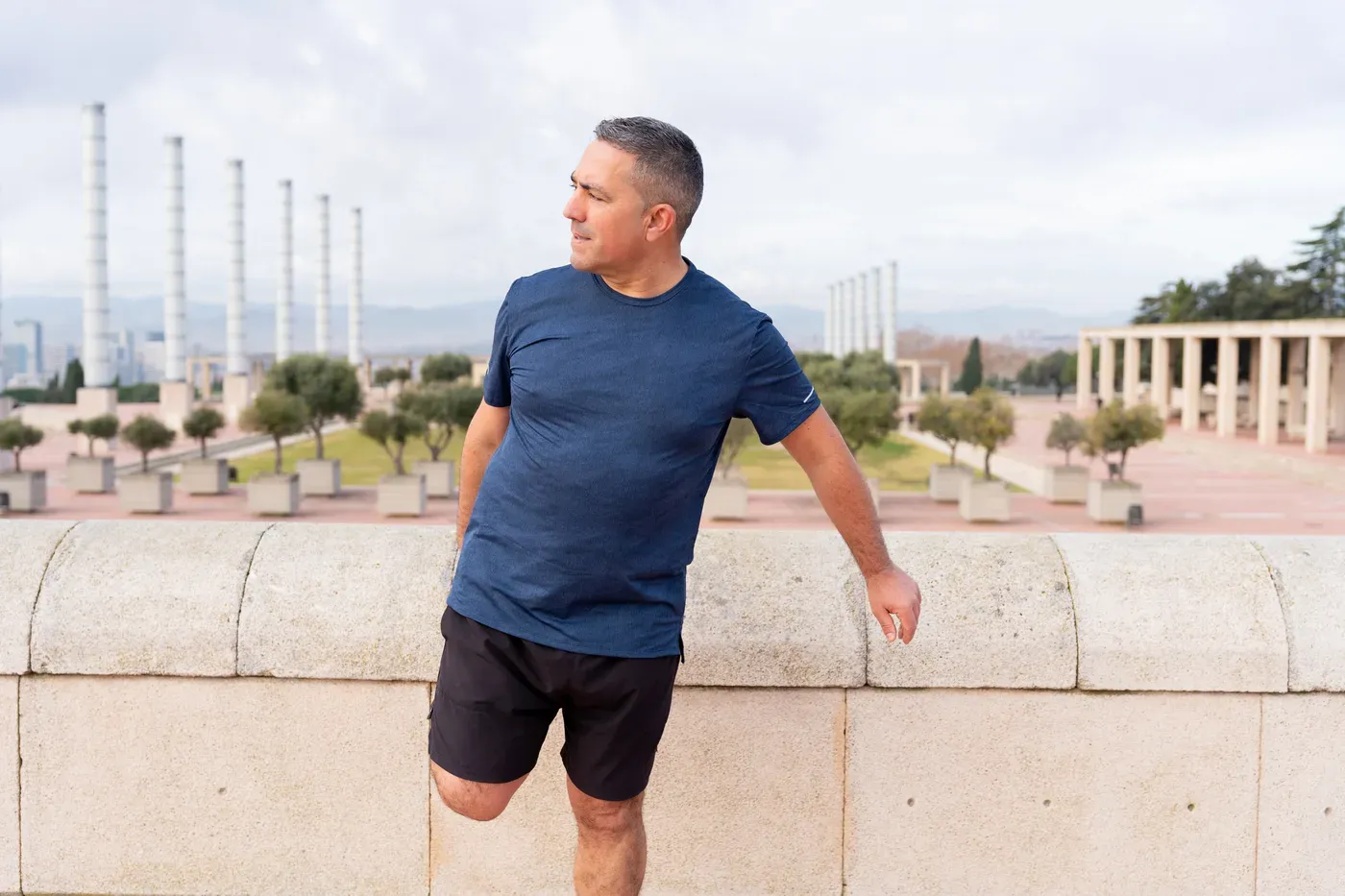 Middle-aged man stretching his quad against a stone wall after a run