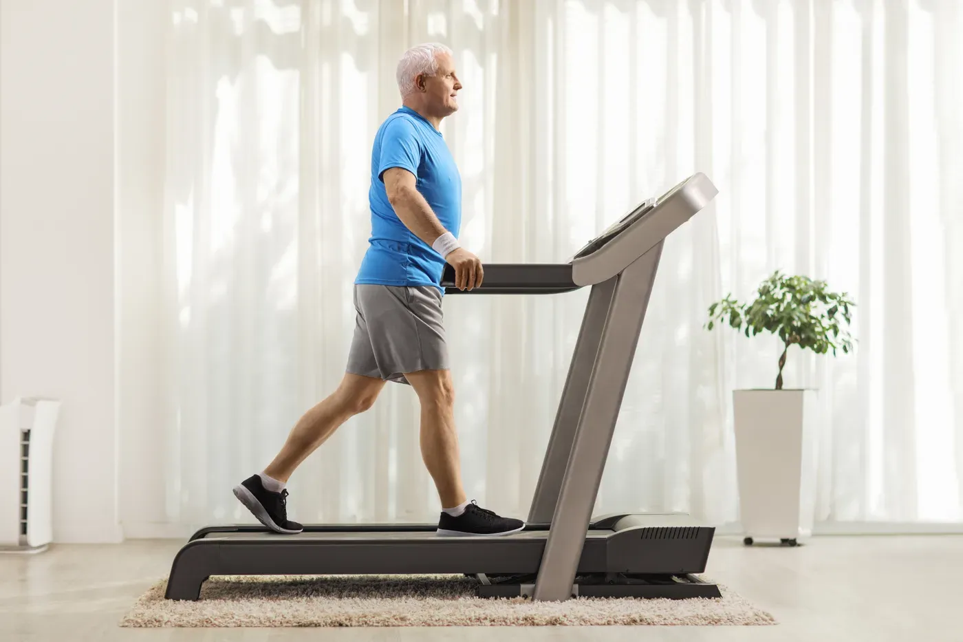 Grey-haired man walking on a treadmill at home
