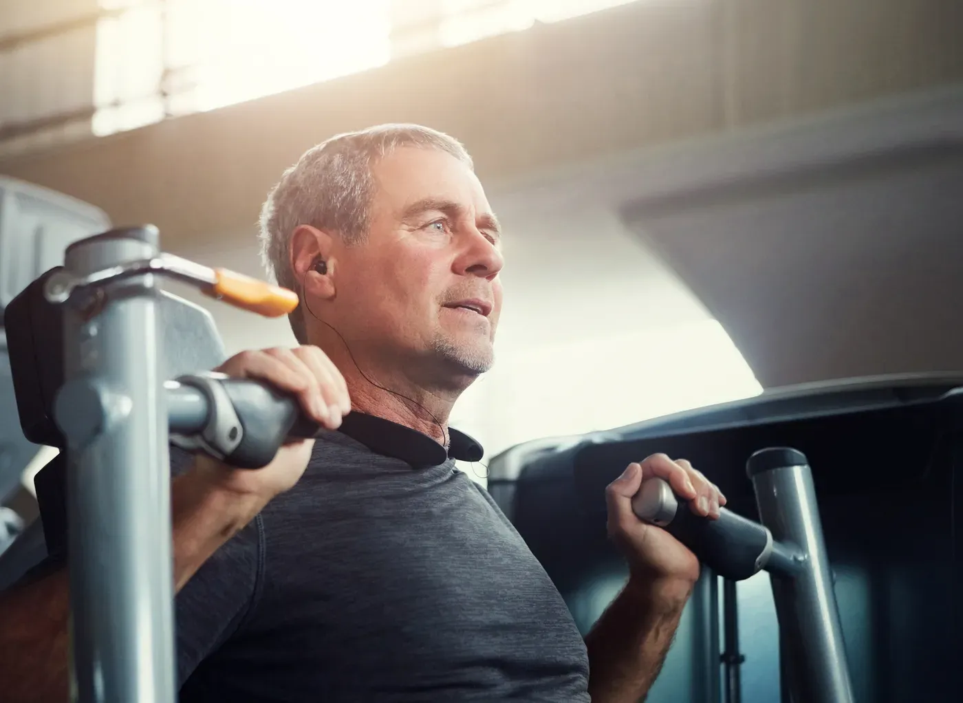 Grey-haired man using a chest press machine in a gym