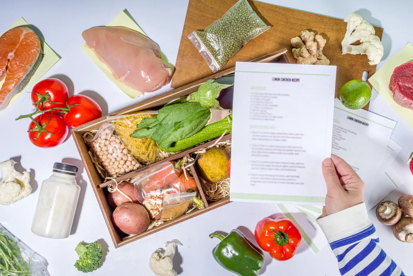 Meal kit box of raw chicken, salmon, vegetables and recipe cards