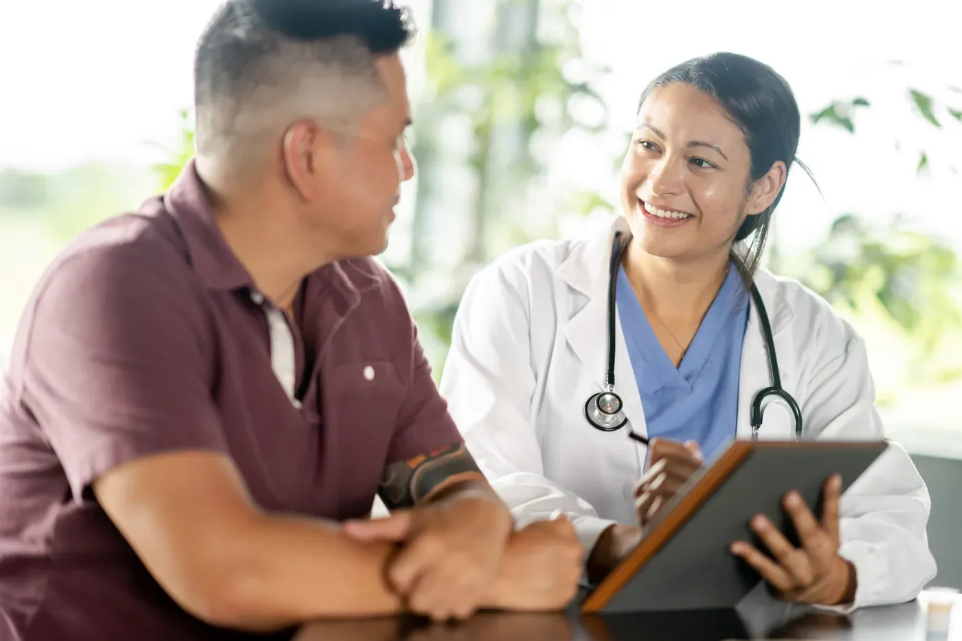 Smiling doctor with a tablet talking with a middle-aged male patient
