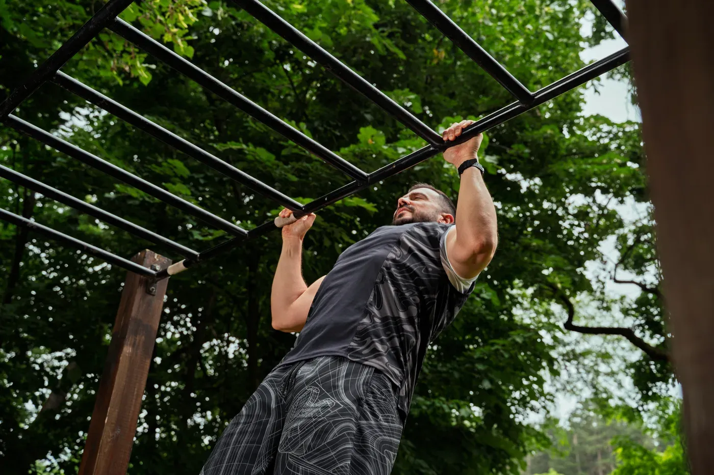 Man doing pull-ups on an outdoor bar frame among trees