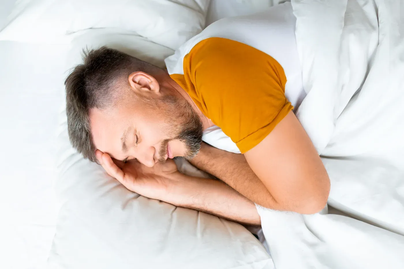 Middle-aged man sleeping on his side in a white bed