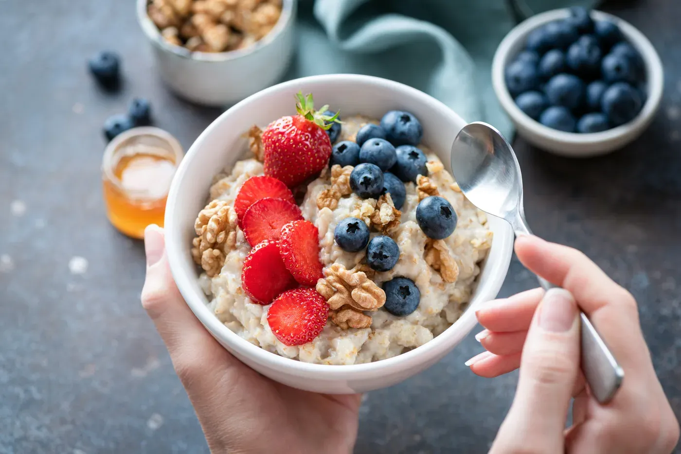 Hands holding a bowl of oatmeal topped with strawberries, blueberries and walnuts