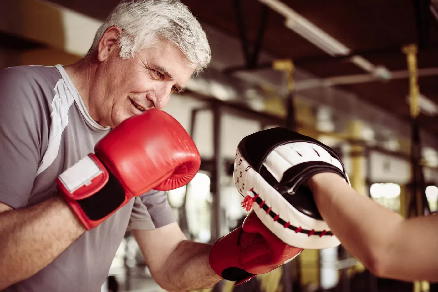 Grey-haired man in boxing gloves punching a trainer’s pad