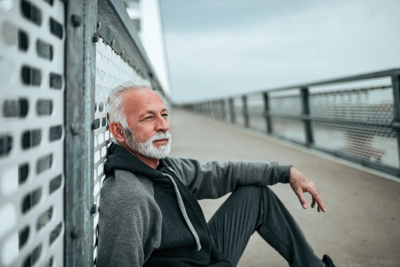 White-bearded man in a hoodie sitting against a railing after exercise