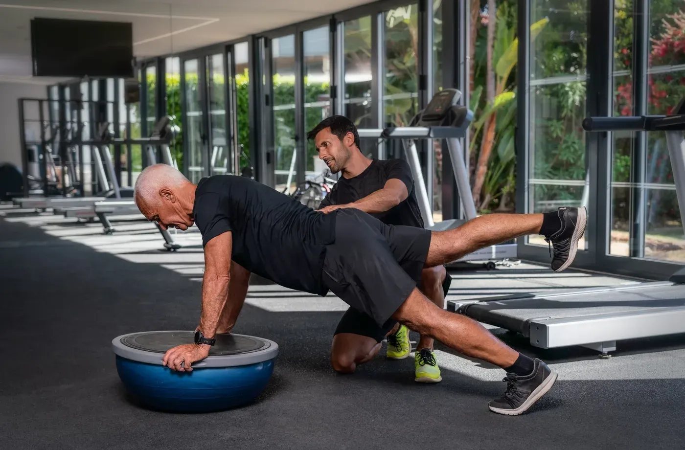 Trainer coaching an older man through a plank on a balance ball