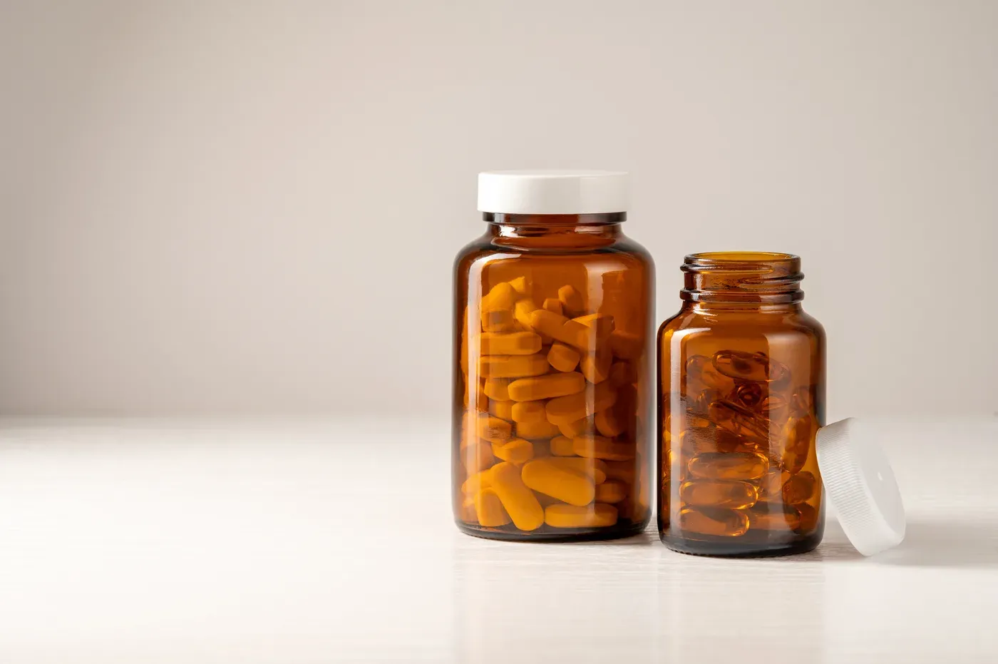 Two amber bottles of fish oil and vitamin capsules on a table