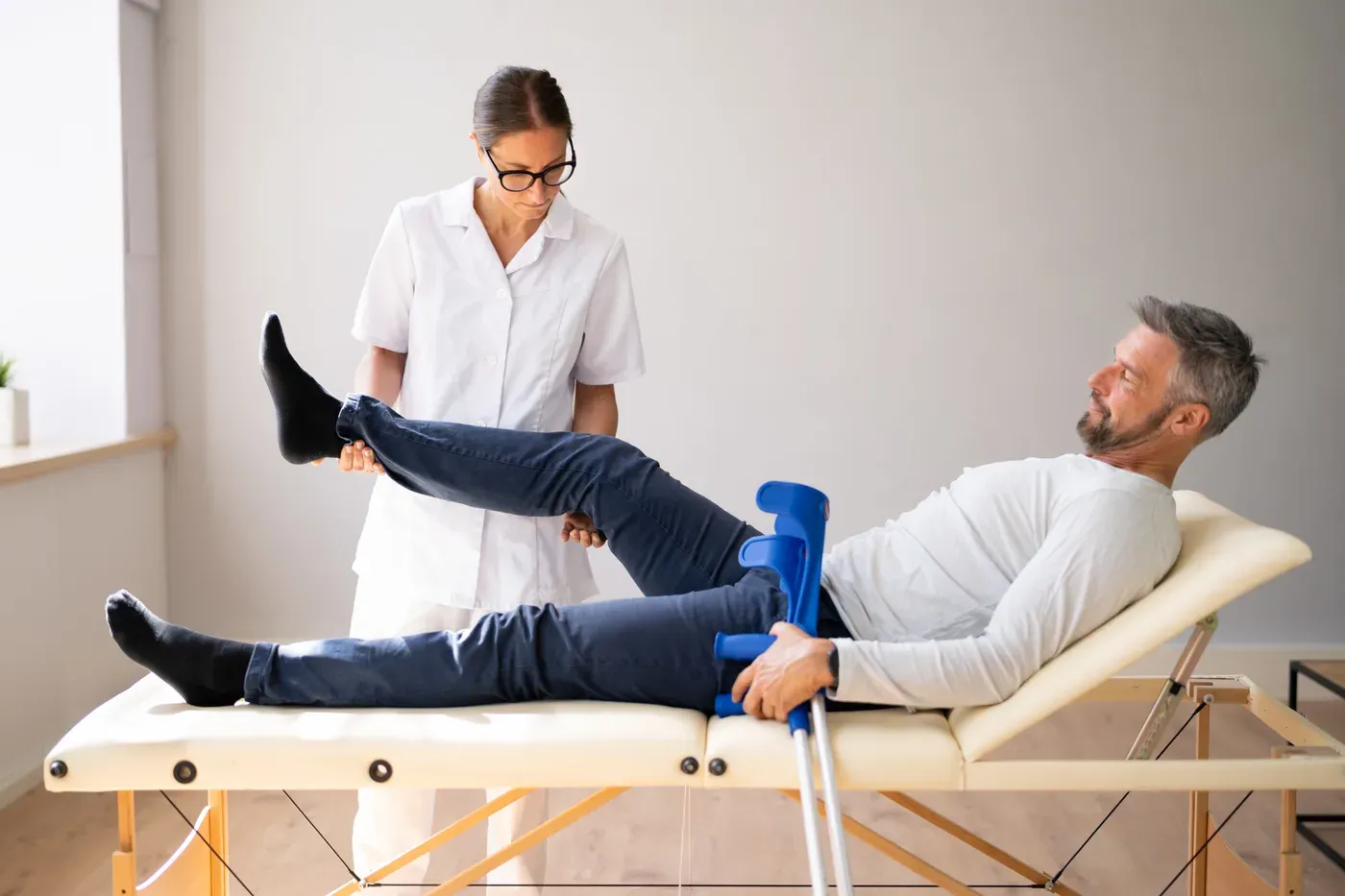 Physiotherapist examining a grey-bearded man’s knee on a treatment table