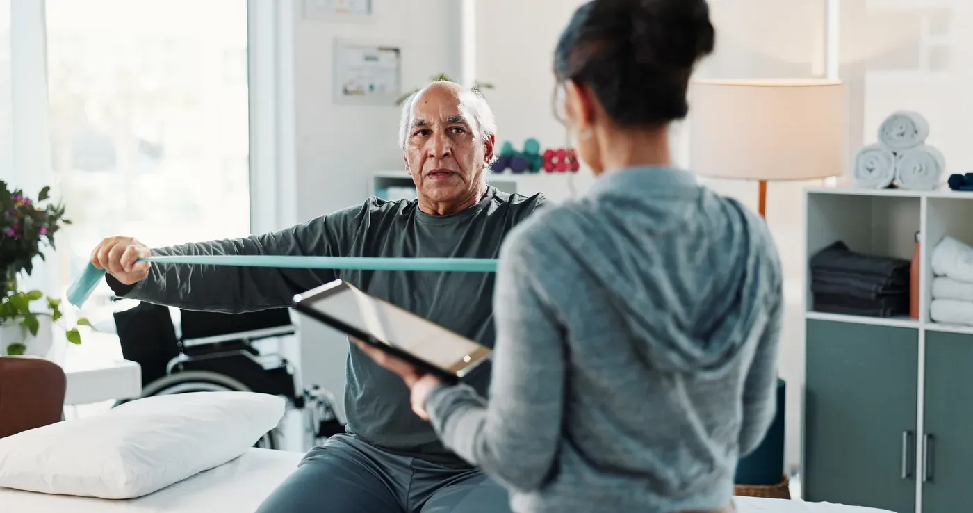 Therapist with a tablet guiding an older man through a resistance band exercise