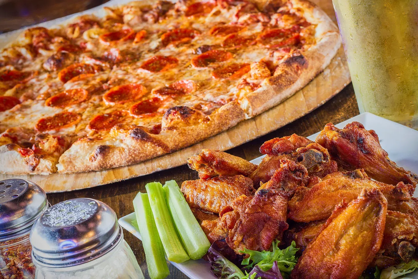 Pepperoni pizza and chicken wings with celery sticks on a table