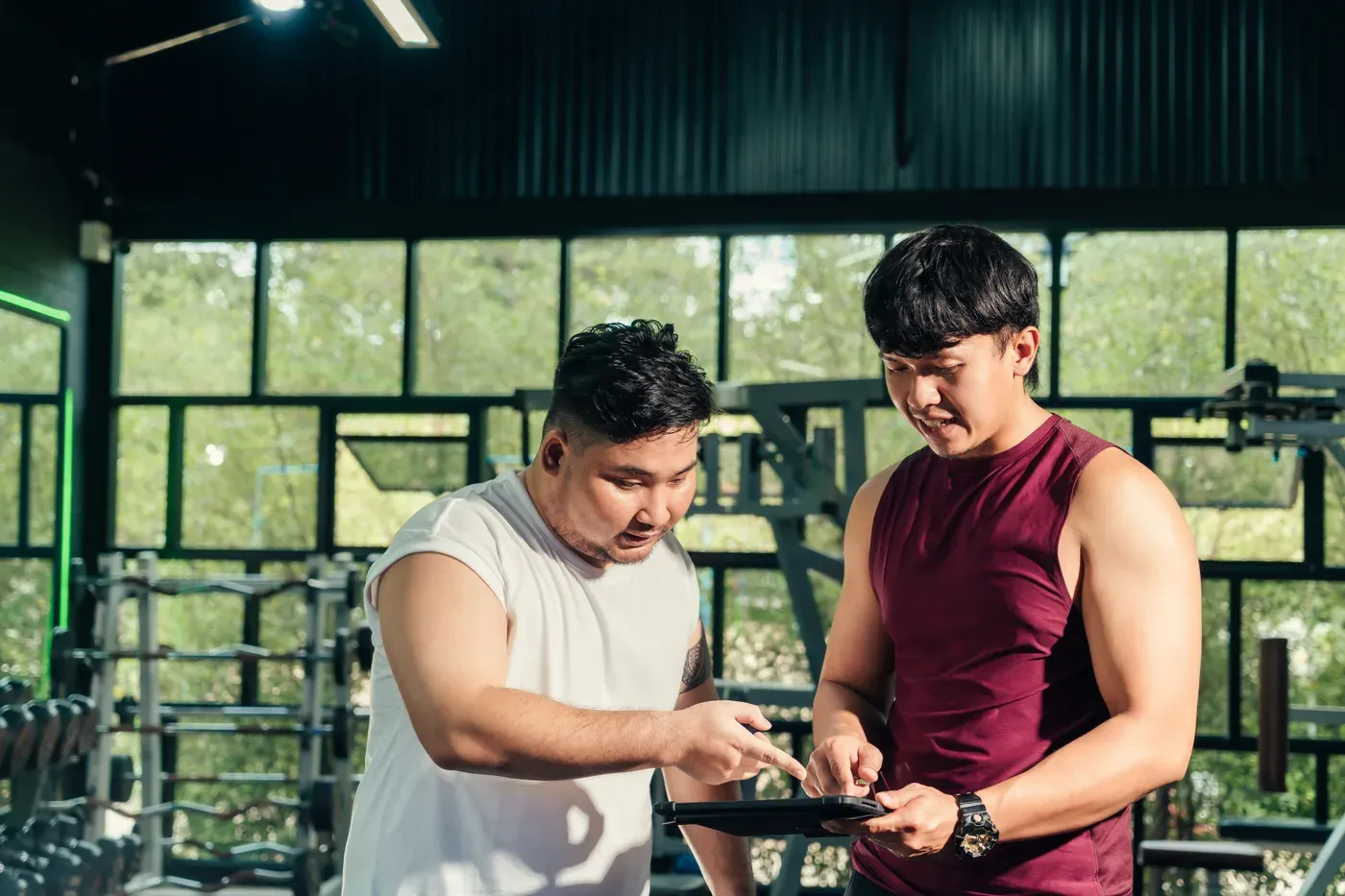 Coach reviewing a tablet with a heavier male client in a gym