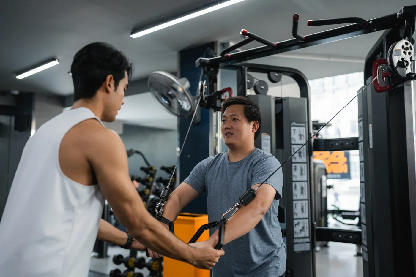 Trainer guiding a man through a cable chest exercise in a gym