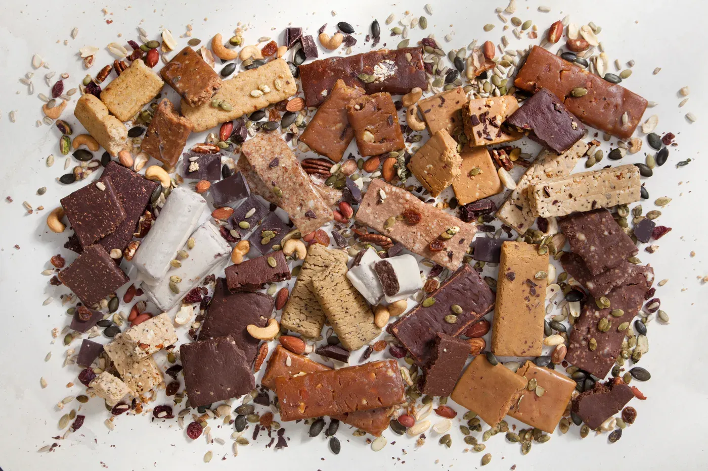 Assorted protein bars scattered with nuts and seeds on a white surface