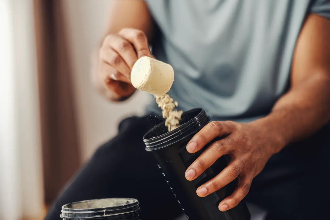 Man pouring a scoop of protein powder into a shaker bottle