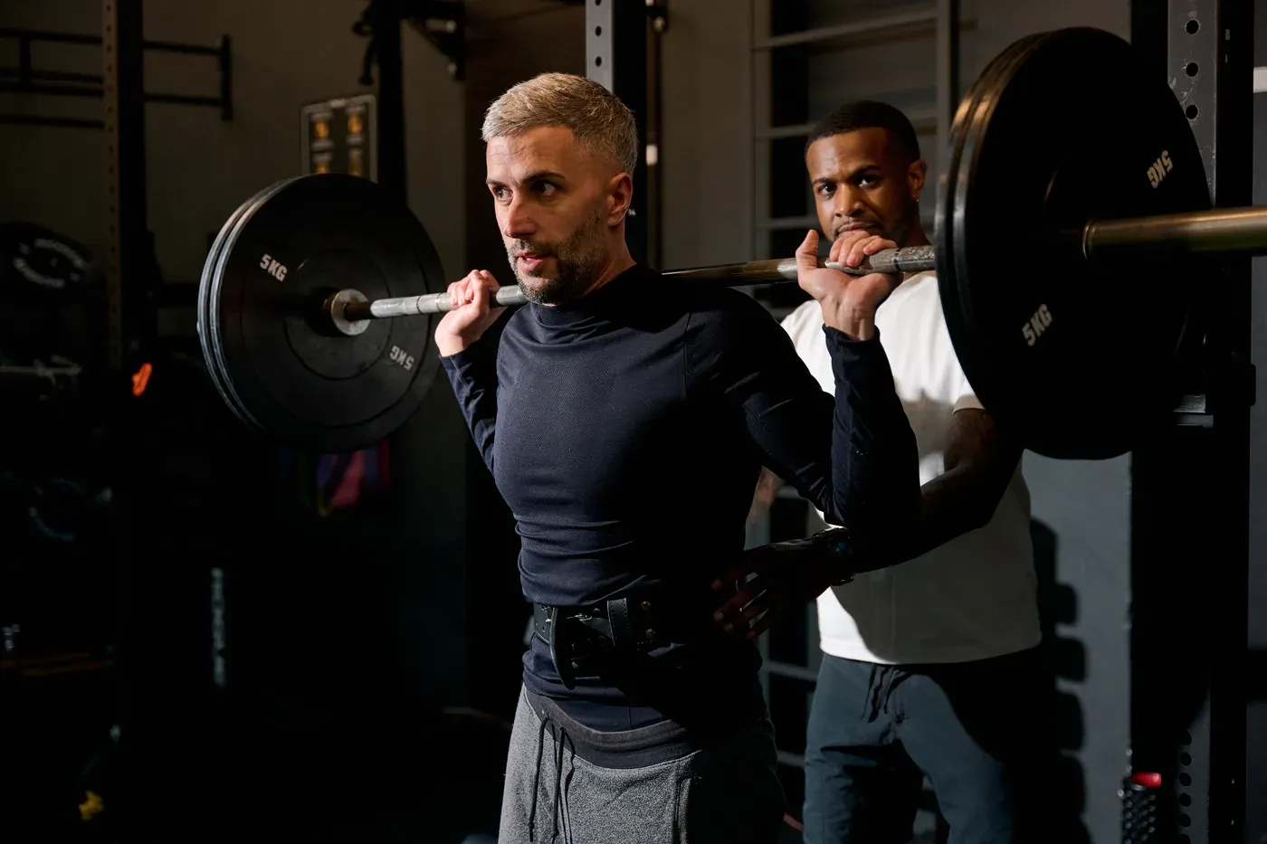 Coach spotting a man in his forties during a barbell back squat
