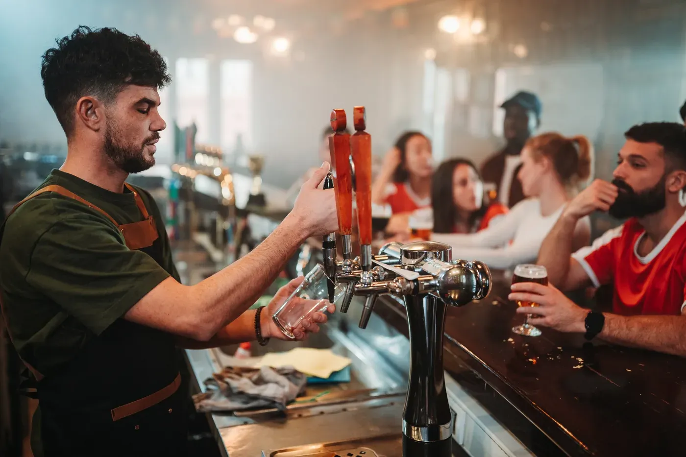 Bartender pulling a draft beer while fans watch a game in a pub