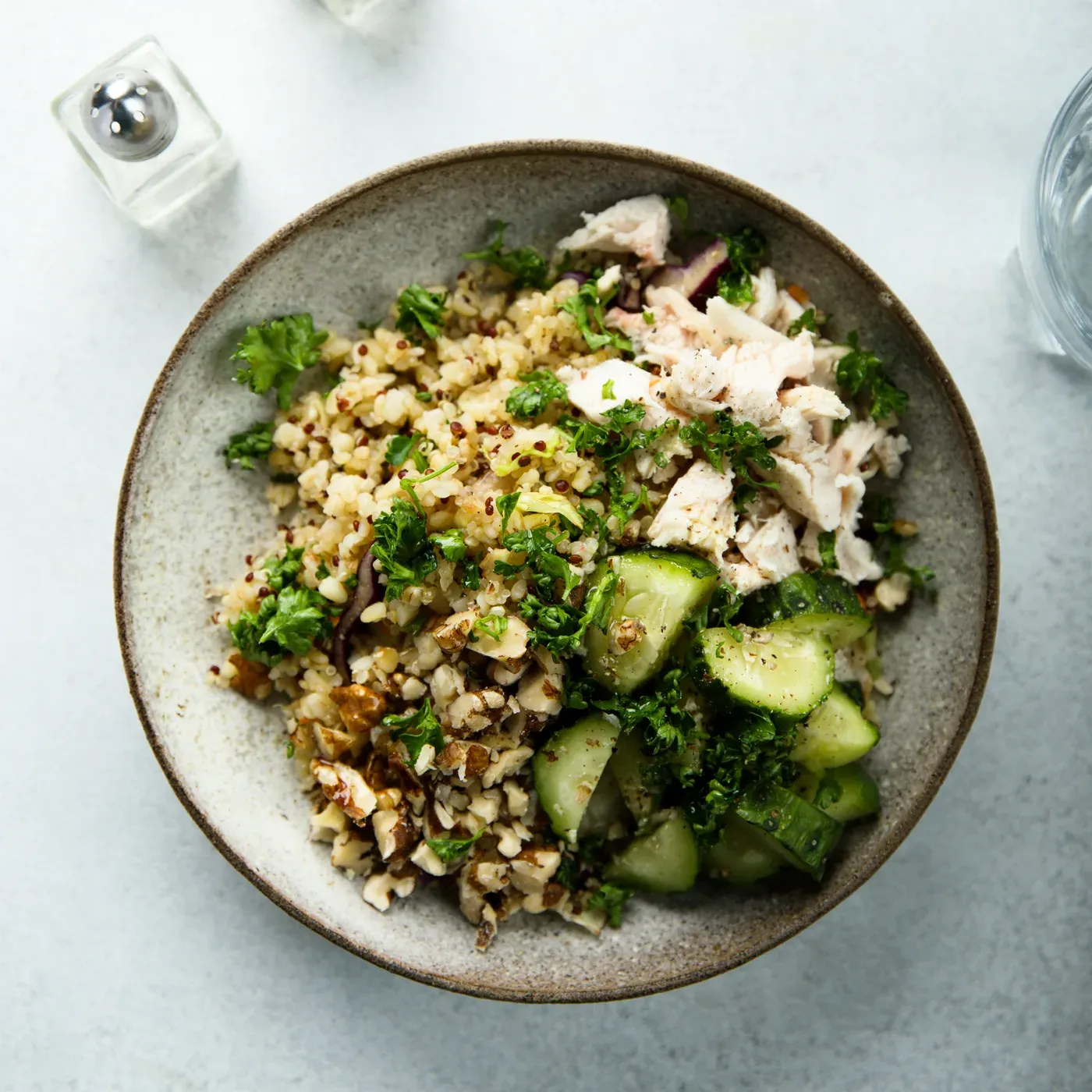 Overhead bowl of quinoa with shredded chicken, cucumber and herbs