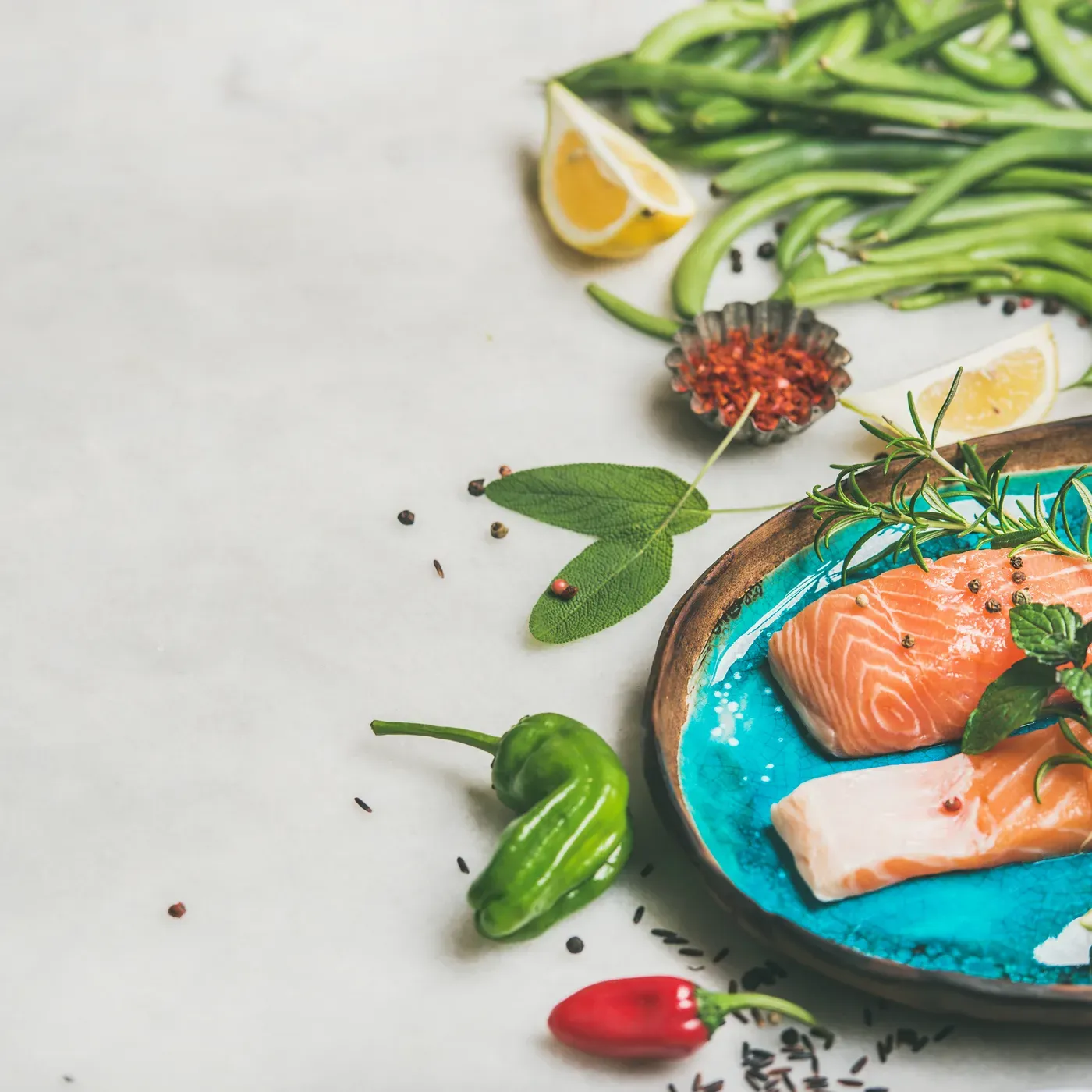 Raw salmon fillets on a blue plate with green beans, peppers and lemon