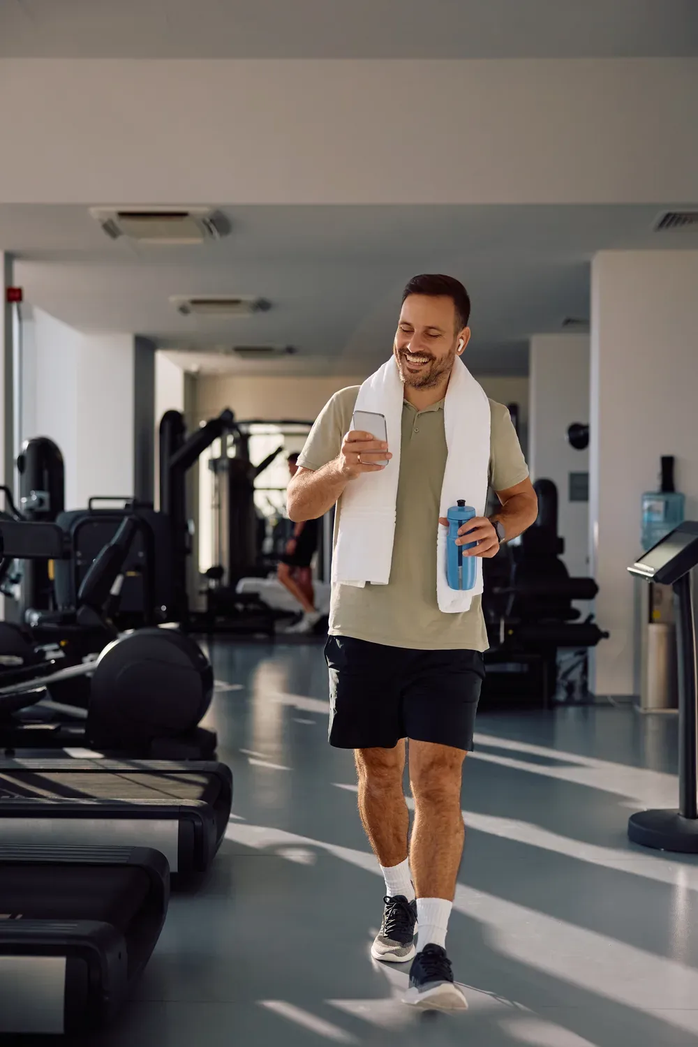 Man walking through a gym with a towel and water bottle after training