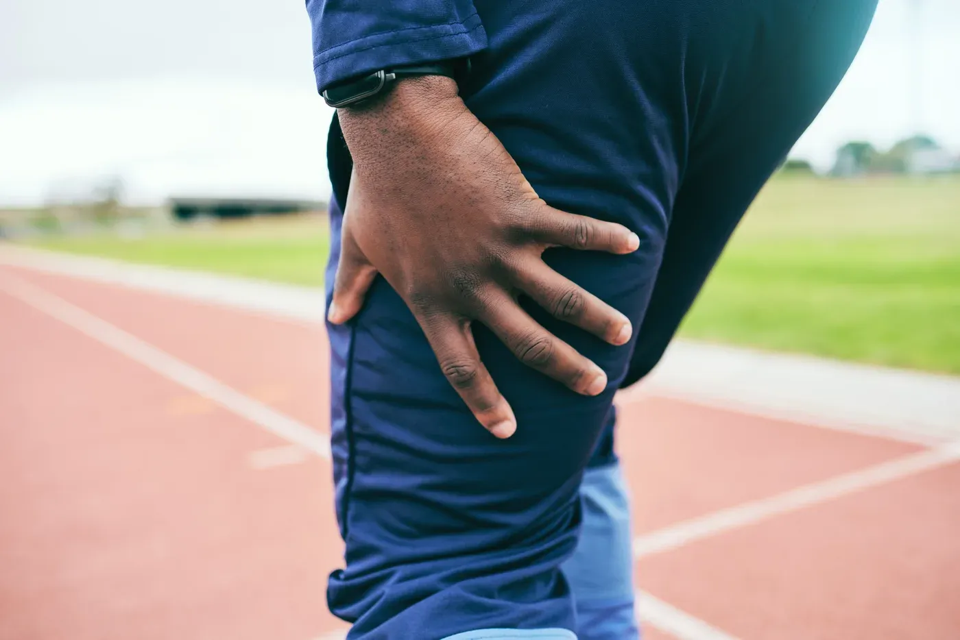 Runner pressing his hand against his sore thigh on a track