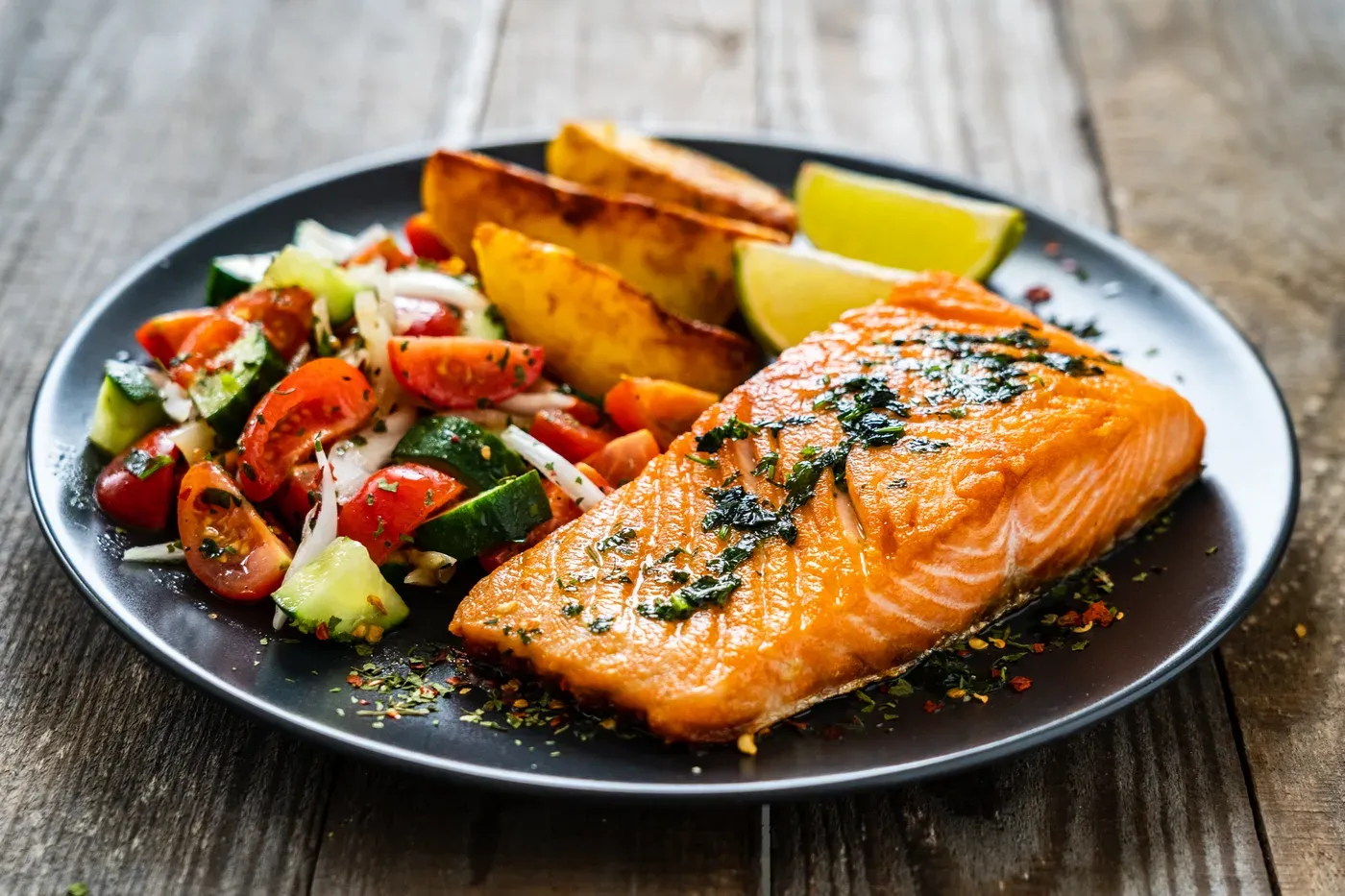 Grilled salmon fillet with roasted potatoes and tomato salad on a dark plate