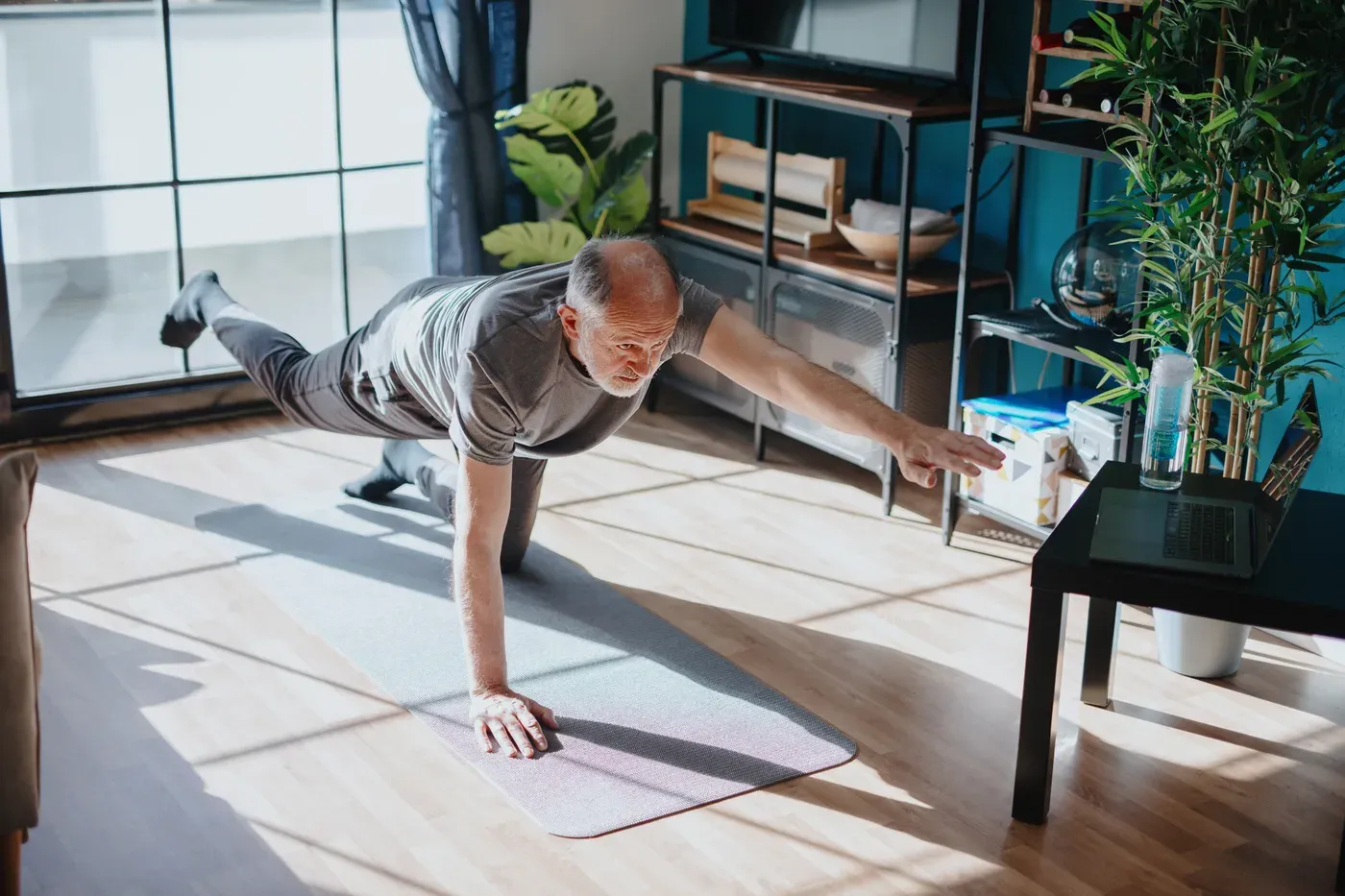 Older man doing a bird-dog balance exercise on a mat at home