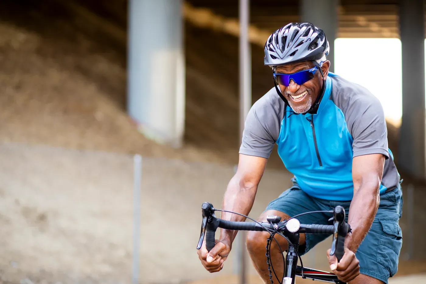 Smiling older man in a helmet and sunglasses riding a road bike