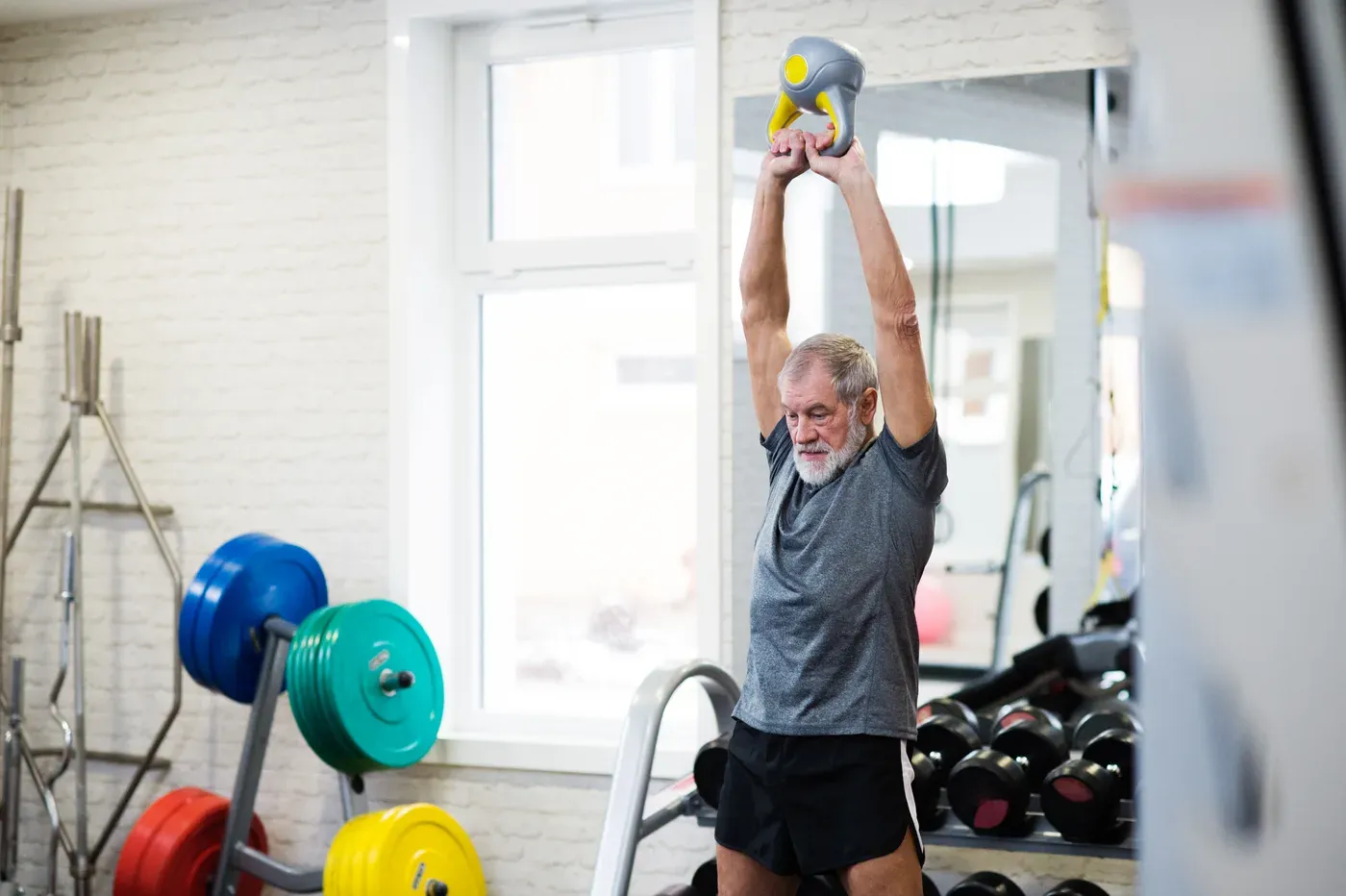 Older man pressing a kettlebell overhead in a small gym