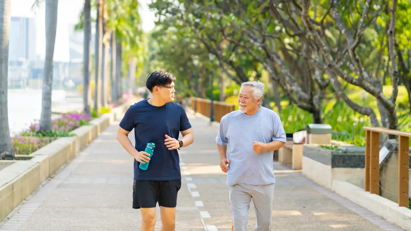 Adult son and his older father jogging together on a park path