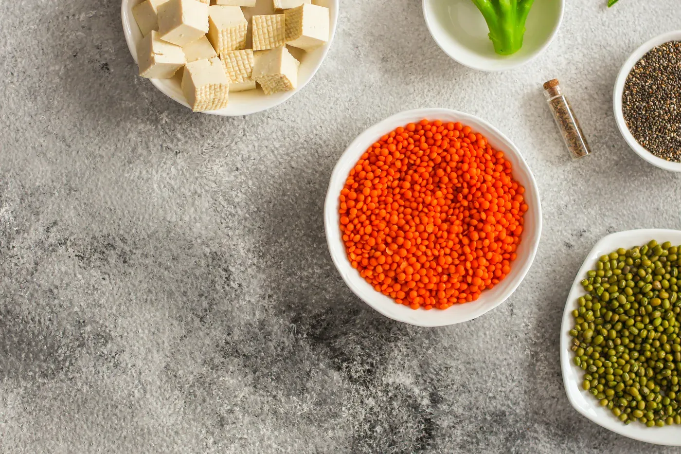 Bowls of tofu, red lentils, mung beans and chia seeds on stone