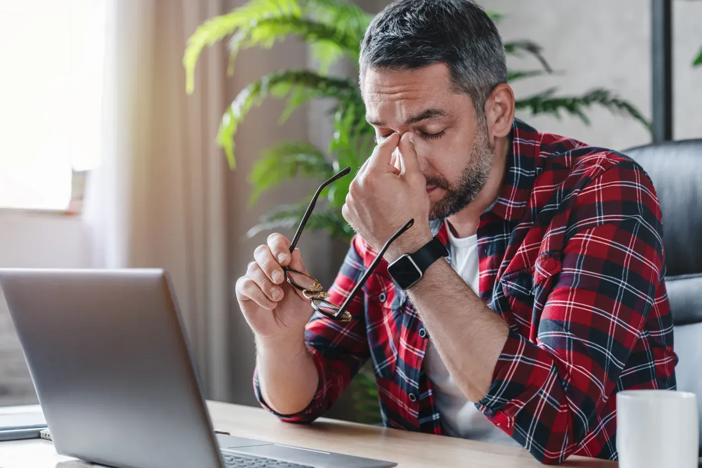 Tired grey-haired man rubbing his eyes at a laptop