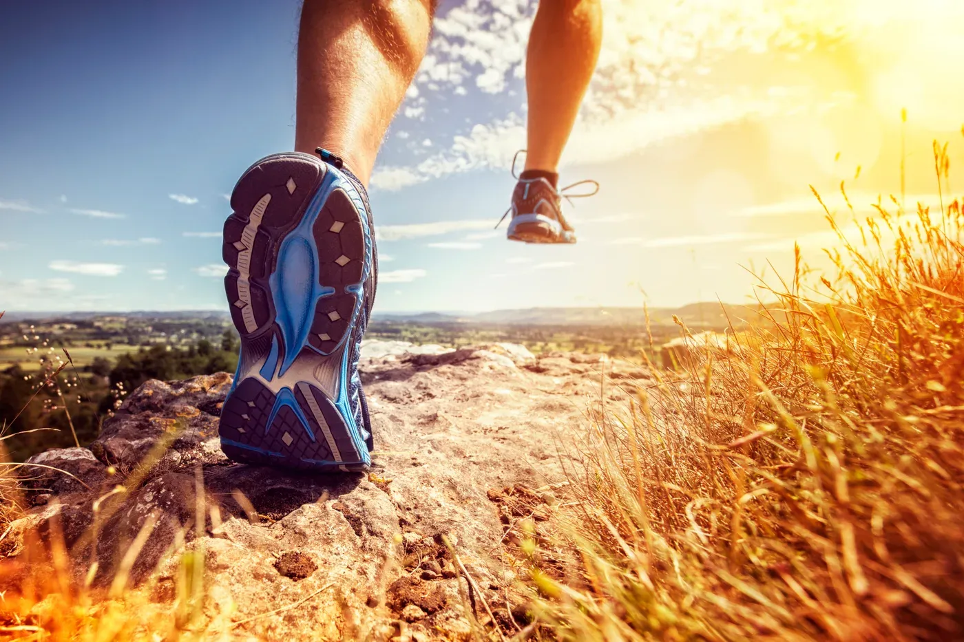 Close-up of a runner’s shoe on a rocky trail in golden light