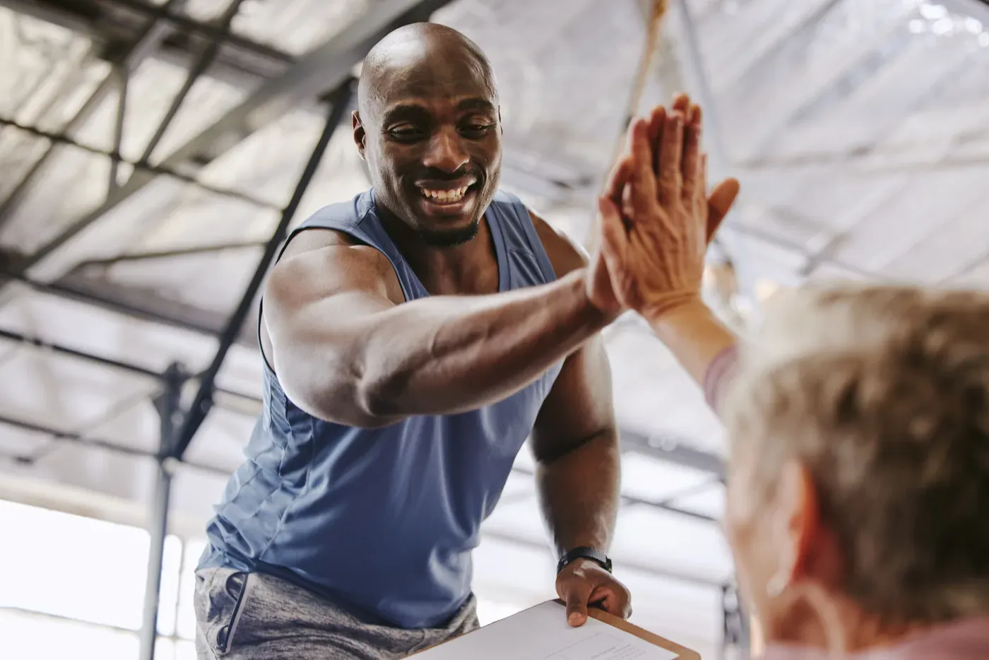 Smiling trainer with a clipboard high-fiving a grey-haired client
