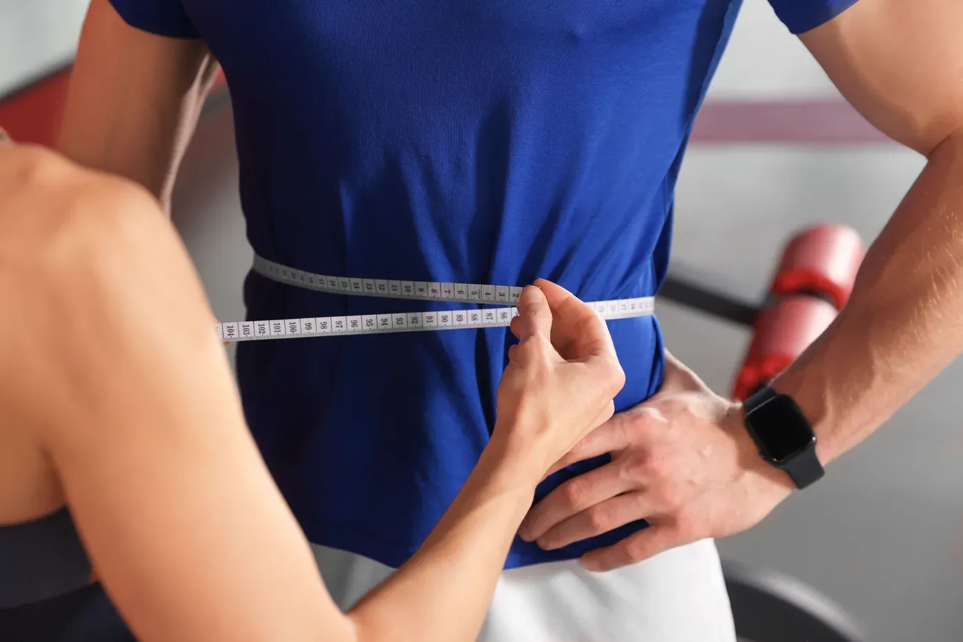 Trainer measuring a man’s waist with a tape in a gym
